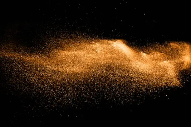 Photo of orange dust particles explosion on black background. Color powder dust splash.