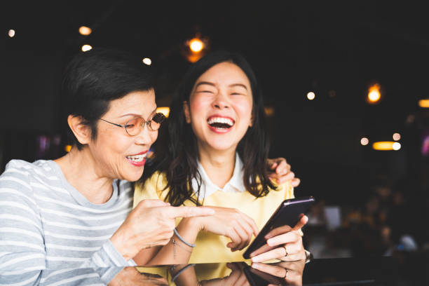 asiatische mutter und tochter lachen und lächeln an einem selfie oder foto-album mit smartphone zusammen im restaurant oder café, mit kopieren raum. familienliebe, urlaubsaktivität oder moderne lifestyle-konzept - ungestellt fotos stock-fotos und bilder