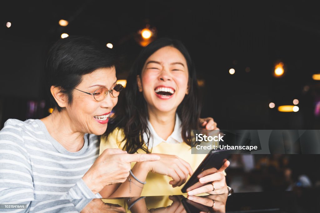 Asia madre e hija riendo y sonriendo en un álbum de foto o selfie, utilizando smartphone juntos en el restaurante o cafetería, con copian espacio. Amor familiar, la actividad de vacaciones o concepto de estilo de vida moderno - Foto de stock de Asia libre de derechos