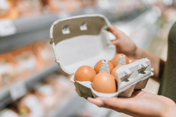 Young woman in store holding cardboard of six organic eggs. Young woman in store holding cardboard of six organic eggs. egg carton stock pictures, royalty-free photos & images