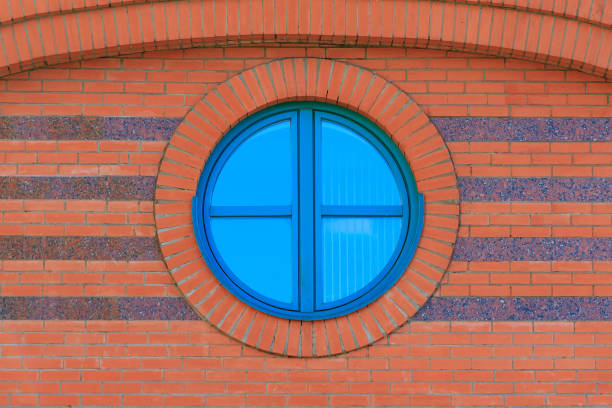 istock Red brick wall with round glassed window with reflection of blue sky 1031566632