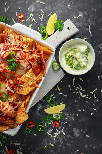 Maxican-style tortilla nachos chips topped with tomato salsa, sliced chilies and melted cheese served with lemon wedges and avocado yogurt dip.