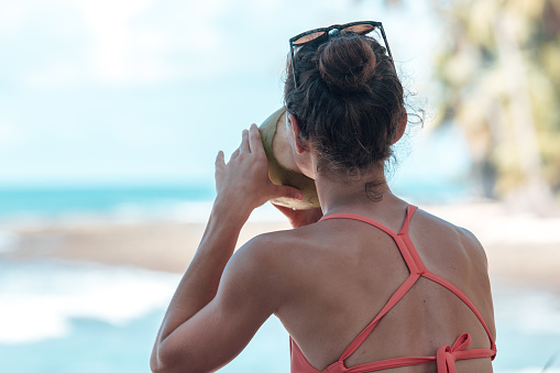 Woman drinking coconut water and looking at waves closeup