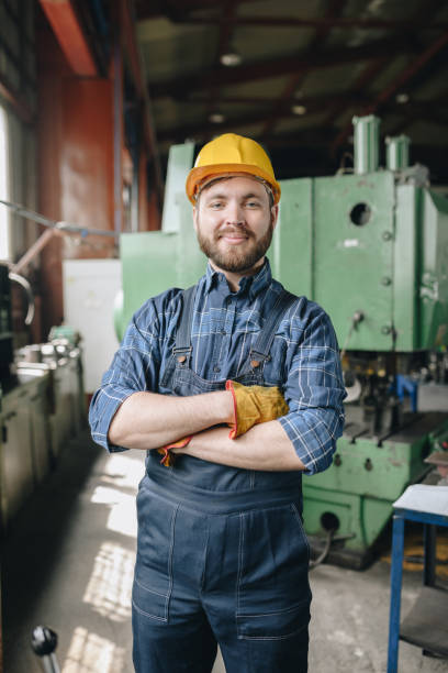istock Content satisfied confident skilled bearded factory worker in hardhat and bib overall crossing arms on chest and looking at camera 1031581124