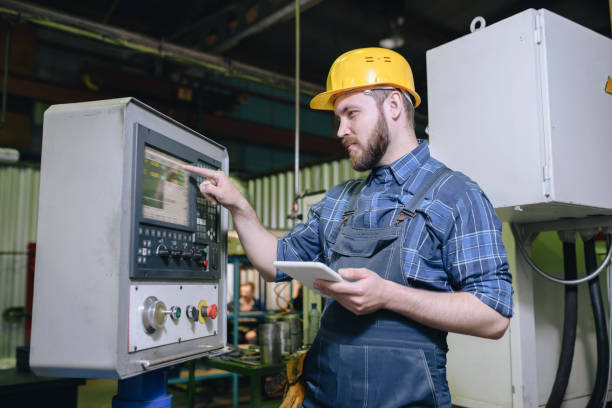 istock Serious concentrated handsome bearded worker in hardhat holding digital tablet and choosing program on monitor of industrial automated machine 1031581134