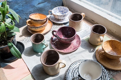 Close-up of window-sill with potted plant and various multicolored ceramic cups with dishes