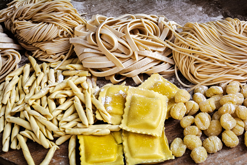 Retro styled photograph of flour blushed spaghetti, tagliatelle, fettuccine, linguine, ravioli on an old wooden table