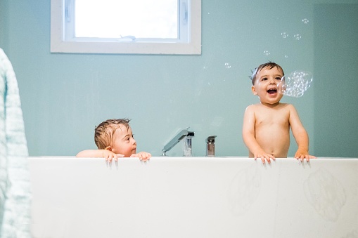 Down's syndrome sweet boy in the bath with his two years old brother. He has blue eyes and blond hair. They have fun and play with the water.  THey have cute face. The color and horizontal Photo was taken in Quebec Canada. There is copy space in this picture.