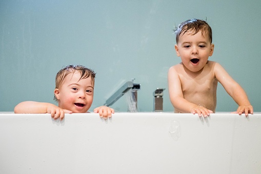 Down's syndrome sweet boy in the bath with his two years old brother. He has blue eyes and blond hair. They have fun and play with the water.  THey have cute face. The color and horizontal Photo was taken in Quebec Canada. There is copy space in this picture.