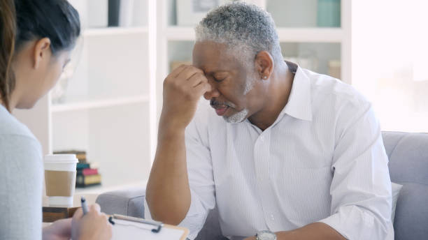 Distraught senior man meets with mental health professional Depressed senior African American man has is head in his hands with discussing hard issues with a female mental health professional. information overload photos stock pictures, royalty-free photos & images
