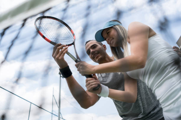 istock Male coach teaching a female tennis player something while holding the racket 1031630754