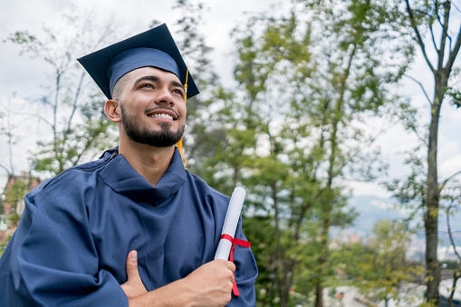 Latin american young man very happy after receiving his diploma looking away with arms crossed and smiling