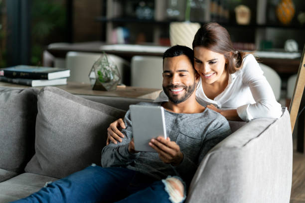 istock Loving woman leaning on couch while man is relaxing on the couch and holding a tablet while they look at photos 1031637748
