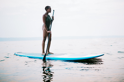 A young adult woman floats on her standup paddleboard in the salt water of the Puget Sound, an inlet of the Pacific Ocean in Washington state, in the United States.