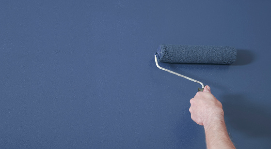Person painting a wall blue with a paint roller.