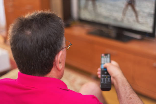 istock Back view of senior man watching tv holding remote control 1031663842
