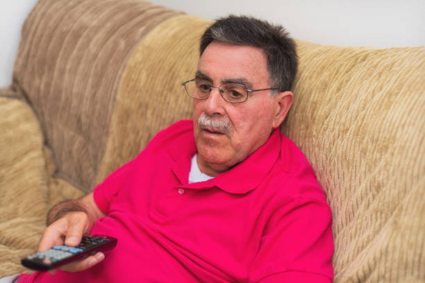 istock Senior man with remote control watching Tv on sofa at home 1031672176