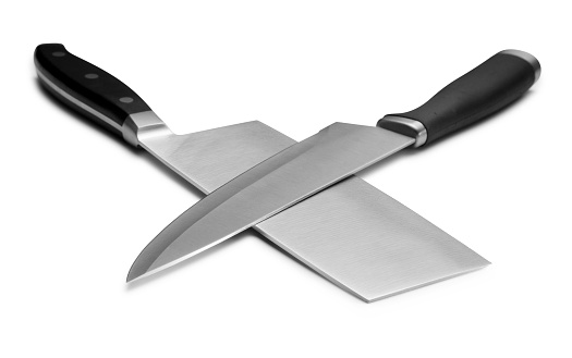 This is a close up photograph of two brand new clean and shiny knives criss crossing each other to form the shape of an x