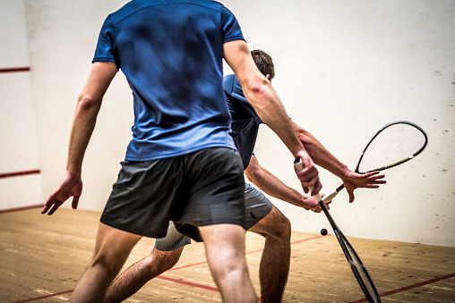 Rear view photo of two men playing squash.
