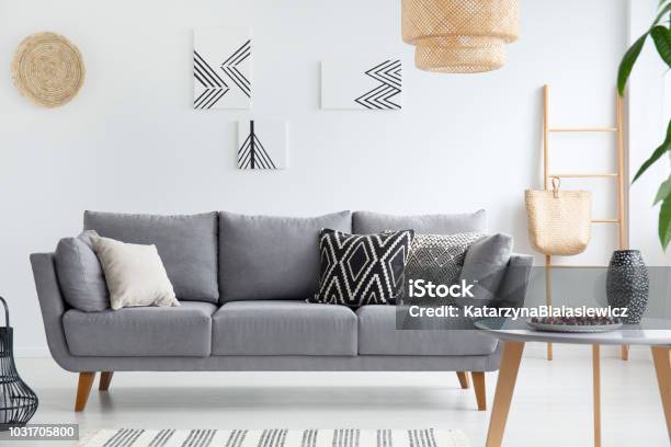 Kissen Grau Sofa Im Weißen Wohnzimmer Interieur Mit Plakaten Lampe Und Holztisch Echtes Foto Stockfoto und mehr Bilder von Sofa