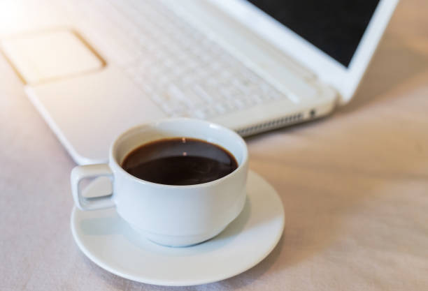 istock Close up hot black coffee in white cup with white laptop 1031725408