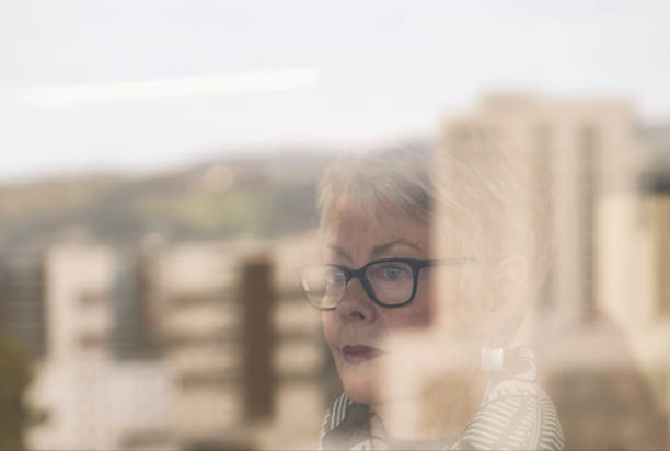 istock Senior Portrait: woman's face seen through apartment window with city reflections (abstract) 1031802718
