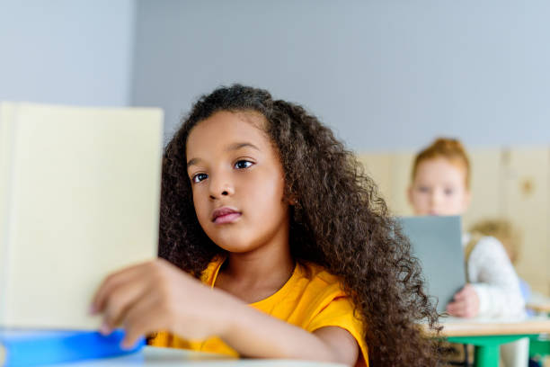 istock focused little schoolgirl reading book during lesson 1031844554