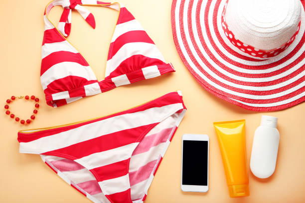 istock Striped swimsuit with hat and cosmetic bottles on orange background 1031855984