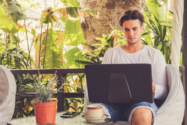 istock Attractive man using laptop and drinking coffee outdoors. 1031856484