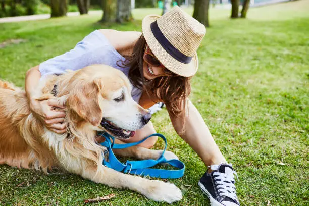 Photo of Young woman sitting on the ground with her dog in the park during summer