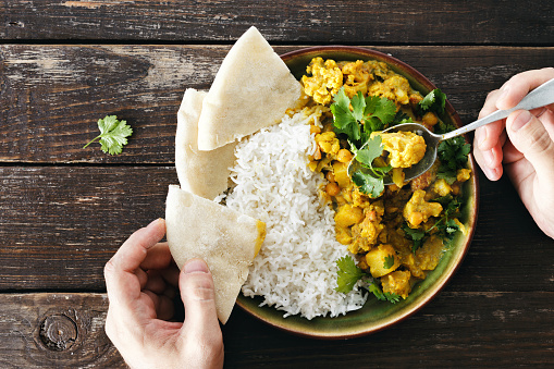 Man eats cauliflower spicy curry with rice and naan bread top view