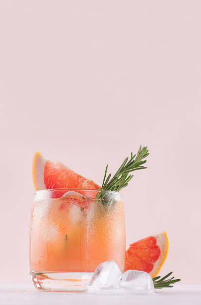 istock Cold grapefruit alcohol cocktail in misted glass with rosemary and grapefruits slice closeup on pastel fashion pink background, vertical. 1031873672