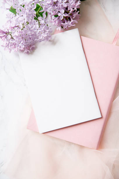istock Top vew composition with feminine workspace mock up with empty card, lilac flowers and pink notebook on marble background 1031876750