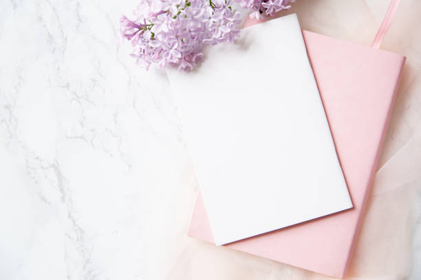 istock Top vew composition with feminine workspace mock up with empty card, lilac flowers and pink notebook on marble background 1031876754