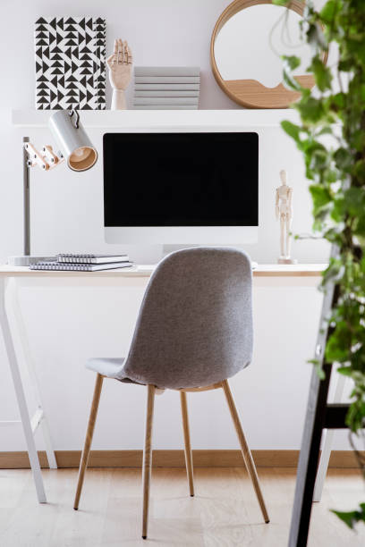 istock Grey chair at desk with lamp and desktop computer in simple white workspace interior. Real photo 1031886730