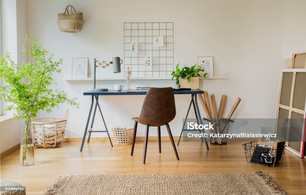 Brown chair at desk with plants and lamp in white workspace interior with carpet. Real photo Home Decor Stock Photo