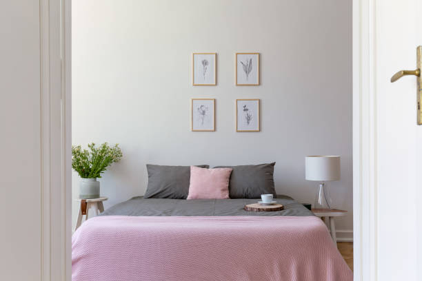 istock A view through an open door into a pastel bedroom interior with ashy bedding and rosy blanket on a double bed. Nature illustrations on the wall. Real photo. 1031897044