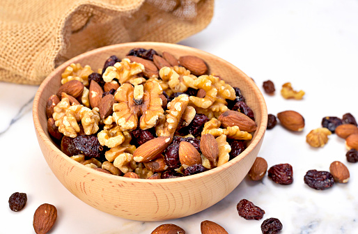 Delicious nuts arrangement in a wooden bowl. Close up shot of various nuts, healthy eating scene and marble background. Top view.