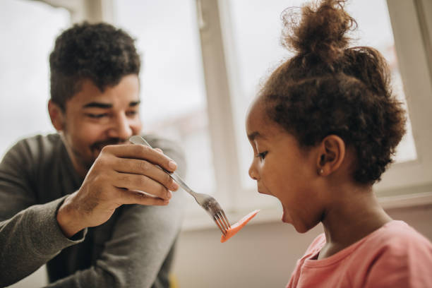 istock Small black girl being fed with a carrot by her father. 1031904204