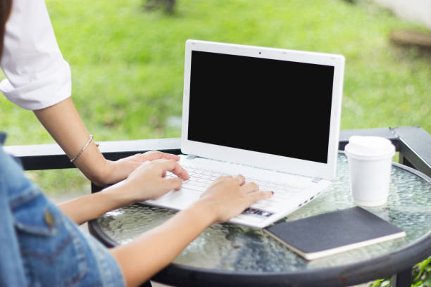 istock Two woman are seeing laptop on glass table while typing on pad with black note and coffee paper cup in green grass background. The modern and smart methode in present about online transaction. 1031904526