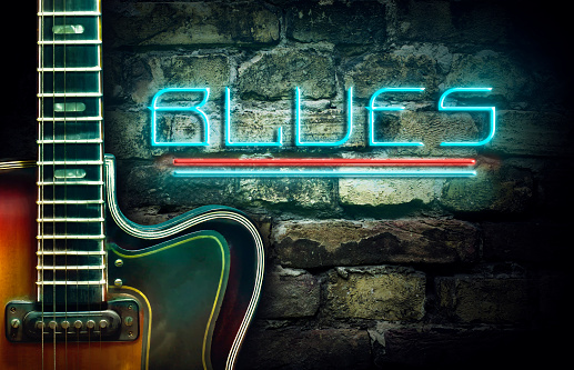 Vintage guitar and a neon inscription Blues on the background of an old brick wall. Concept music.