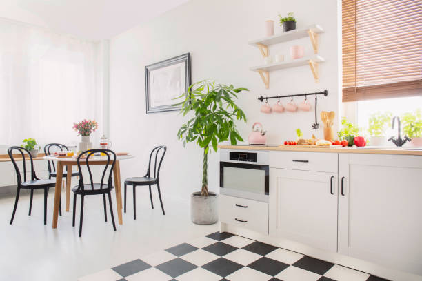istock Black chairs at dining table with flowers in white flat interior with plant next to kitchenette. Real photo 1031928790