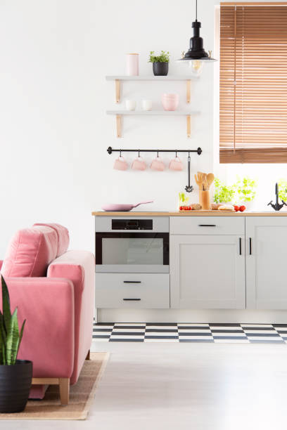 istock Black lamp above grey kitchenette in open space interior with pink sofa and window. Real photo 1031928798