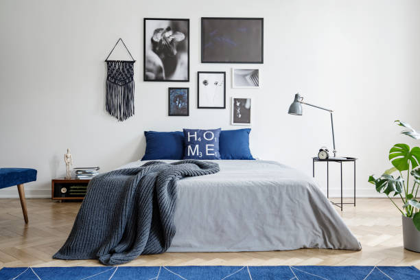 istock Blanket on bed with blue pillows in white bedroom interior with gallery and lamp on table. Real photo 1031933040