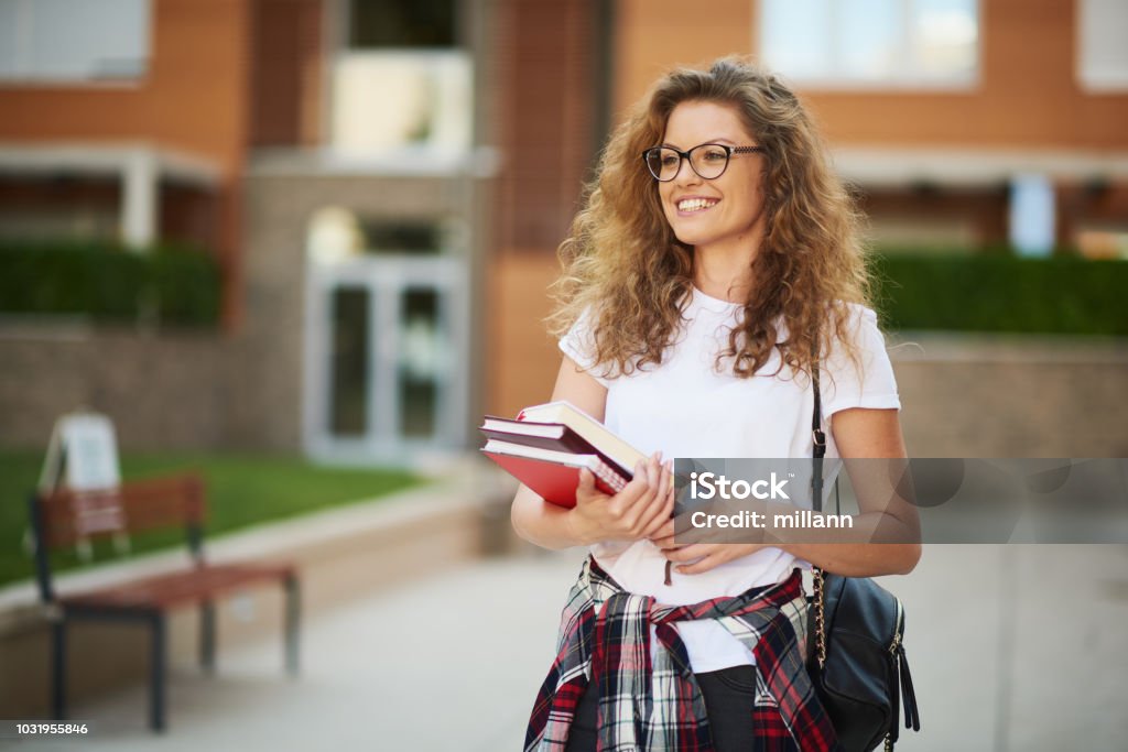 Female student in campus. Female student in campus with books in her arms and bag on shoulder. Student Stock Photo