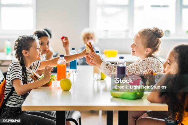 Adorables Colegialas Tomando El Almuerzo En La Cafetería De La Escuela Foto de stock y más banco de imágenes de Educación