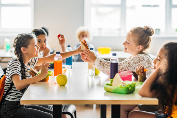 adorable schoolgirls taking lunch at school cafeteria - child food school children eating imagens e fotografias de stock