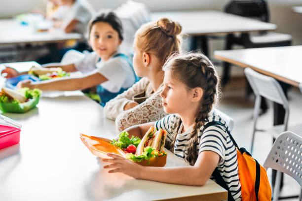 gruppe von schülerinnen daran, mittagessen in der cafeteria der schule zusammen - elementary student school children child schoolboy stock-fotos und bilder