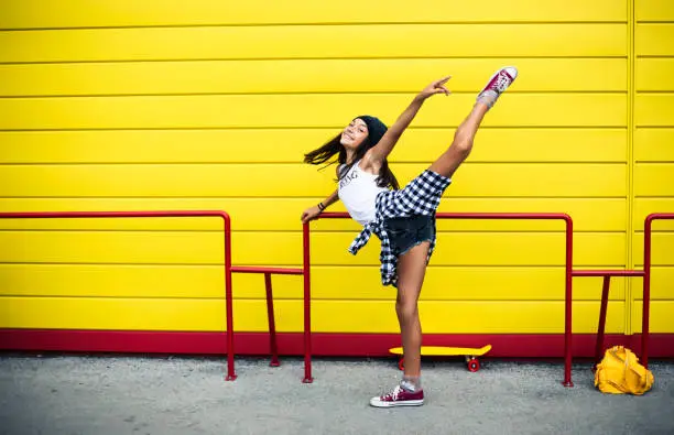 Beautiful dancing teenage girl in front of yellow wall.