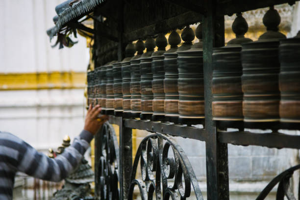 uma pessoa gira uma série de rodas de oração budista no templo swayambhunath em kathmandu, nepal - iron asian culture buddhism buddha - fotografias e filmes do acervo